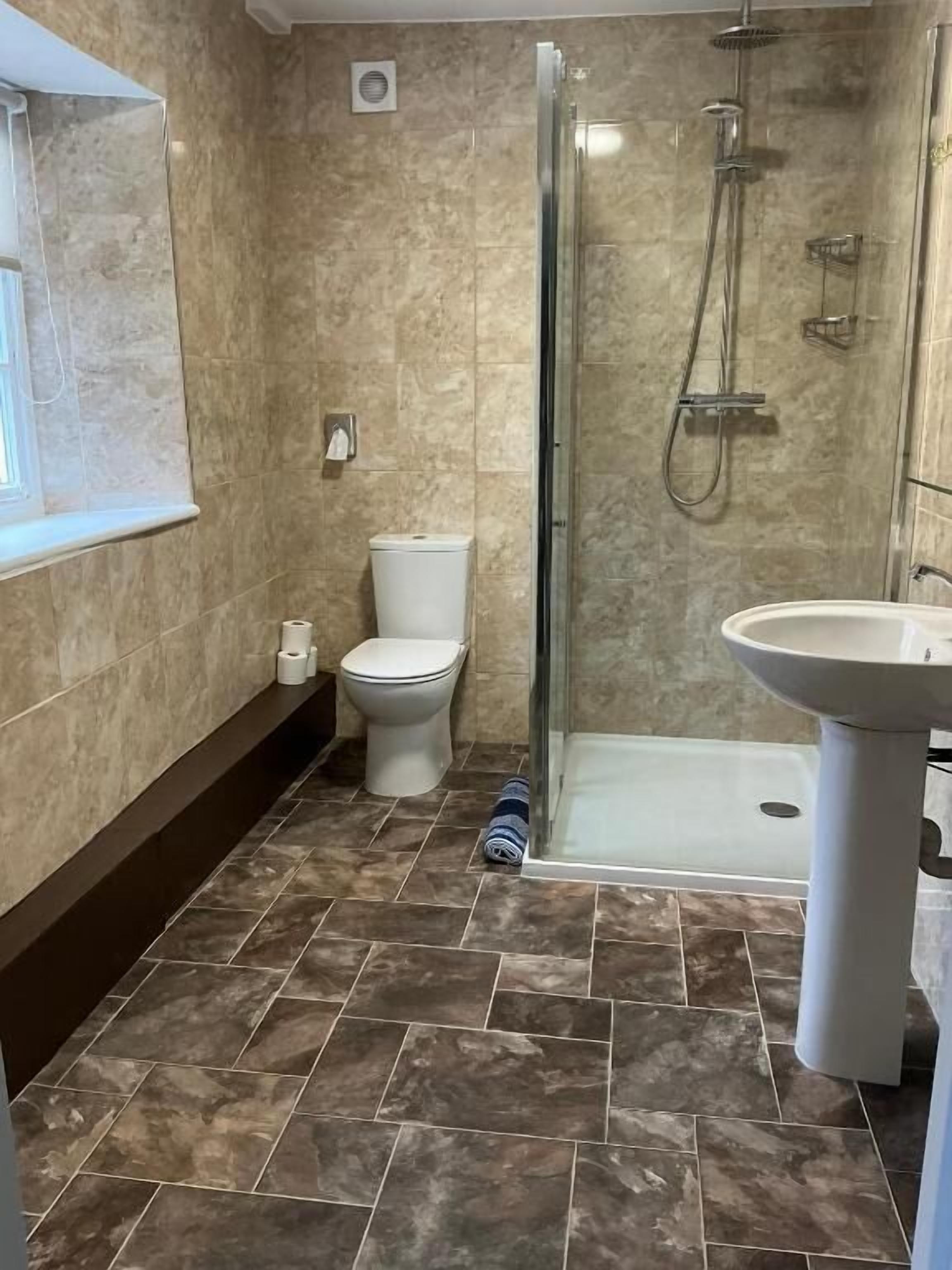 Un baño con ducha de mampara de vidrio, un lavamanos blanco y un inodoro.