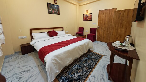 Una habitación de hotel con una cama, dos sillas, un escritorio con un hervidor y un televisor.