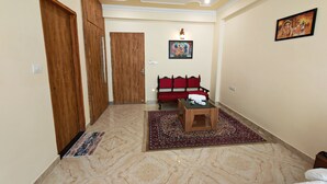 Habitación de hotel con un armario de madera, un sofá rojo, una mesita pequeña y una alfombra estampada.
