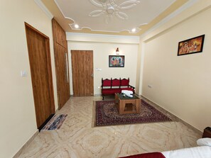 Habitación de hotel con un armario de madera, un sofá rojo, una mesita pequeña y una alfombra estampada.