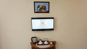 Una habitación con aire acondicionado, un cuadro enmarcado, una pantalla digital y una mesita de madera con una bandeja y objetos.