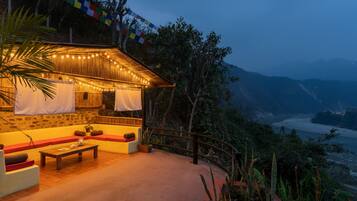 A cozy outdoor seating area with a wooden table and cushions, overlooking a scenic valley.