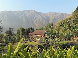A hotel with a red roof, surrounded by lush greenery and mountains in the background. - Summit River Lodge (Kurintar)