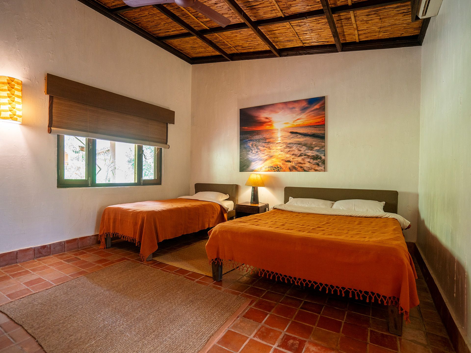 Una camera d'albergo con due letti, un grande quadro raffigurante un tramonto, una finestra con vista e una ventola a soffitto.