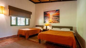 Una camera d'albergo con due letti, un grande quadro raffigurante un tramonto, una finestra con vista e una ventola a soffitto.
