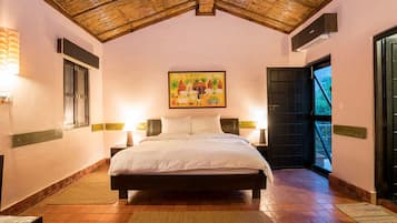 Un dormitorio con cama, lámparas de noche, un cuadro y vistas a través de una puerta abierta.