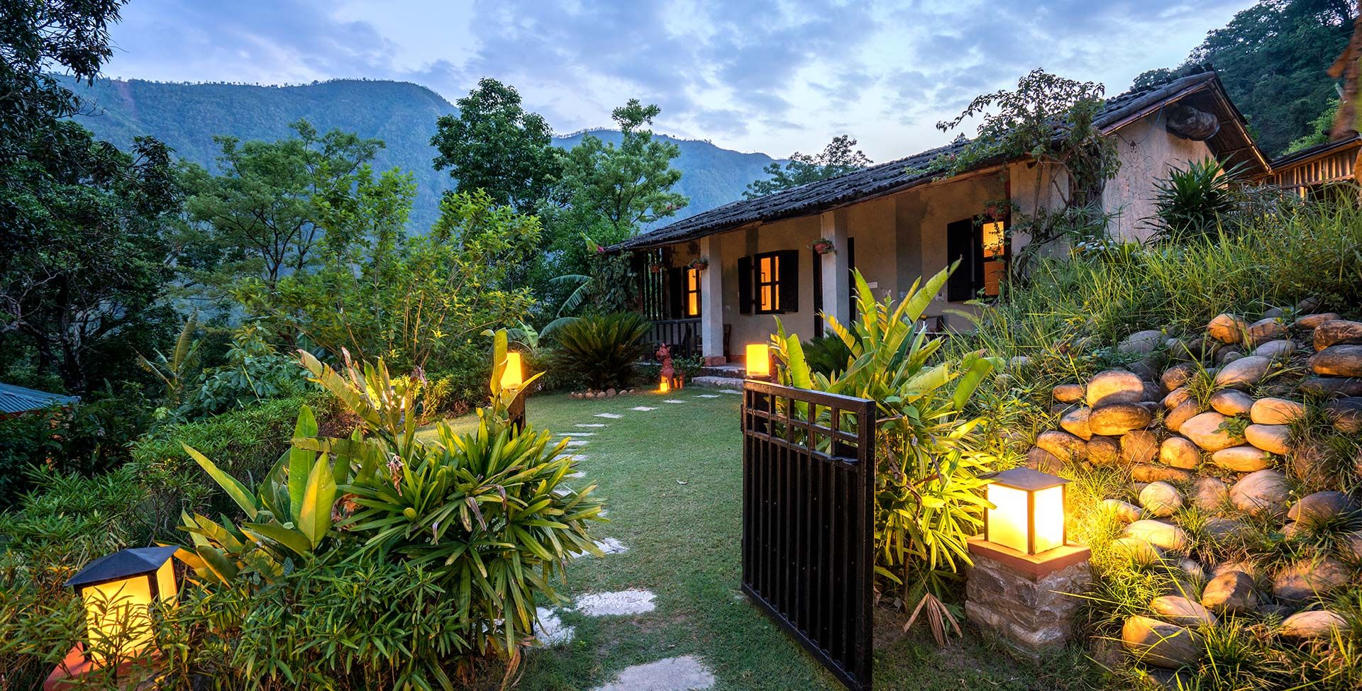 Una casa con jardín, una reja y una montaña al fondo.