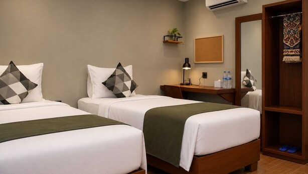 A hotel room with two beds, a desk, a mirror, a wardrobe, and a small plant.