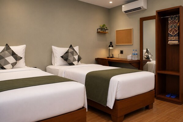 A hotel room with two beds, a desk, a mirror, a wardrobe, and a small plant.