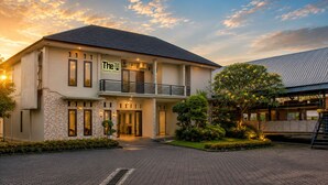 A two-story hotel with a stone facade, a balcony, and a well-maintained garden.
