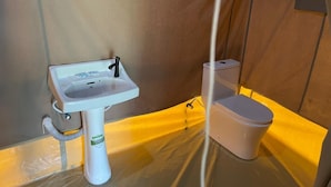 Pieni kylpyhuone, jossa on valkoinen pesuallas ja wc-istuin. Tila on rajattu ruskealla seinällä ja muovilevyillä.