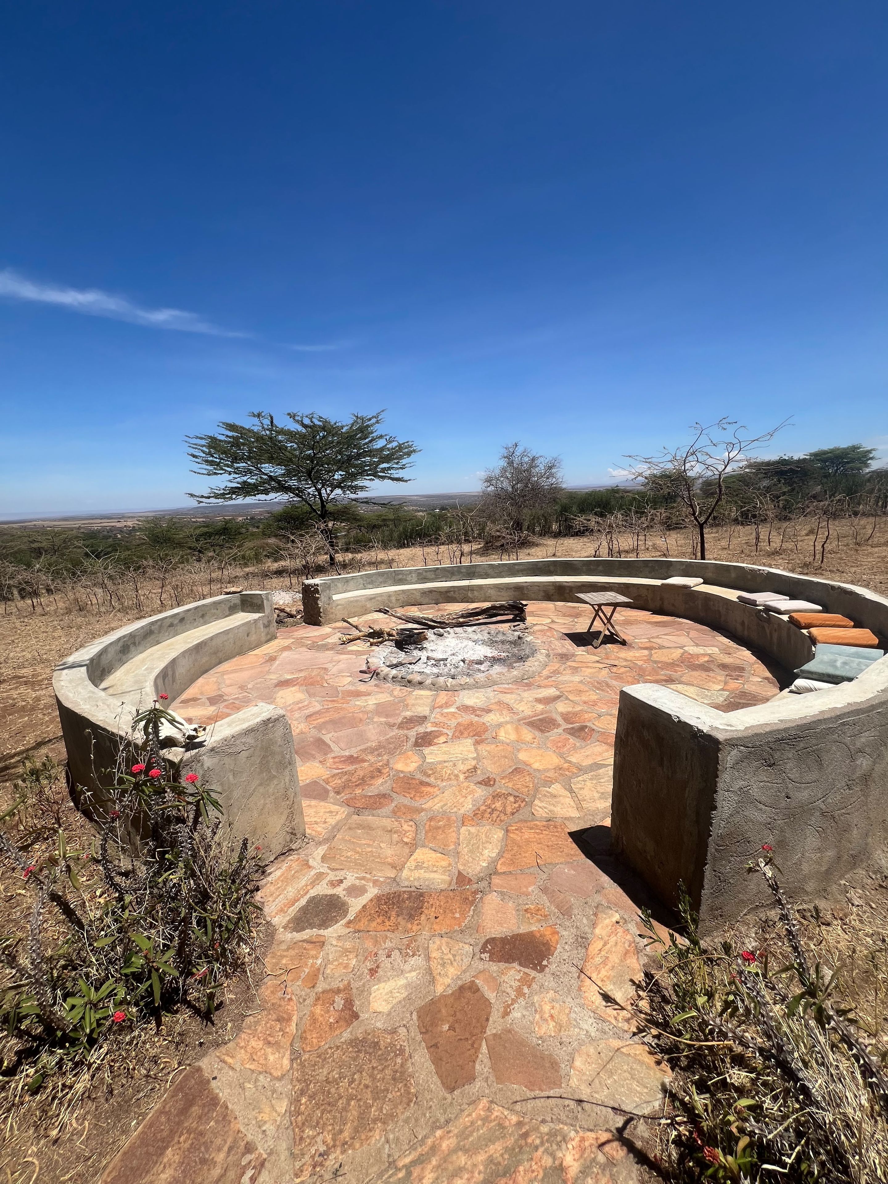 Un área de estar al aire libre con forma circular, que incluye un brasero rodeado por un patio de piedra.