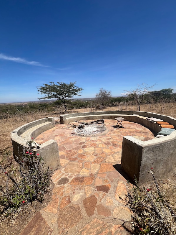 A circular outdoor seating area with a fire pit, surrounded by a stone patio.