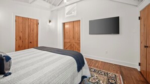 Ein Schlafzimmer mit einem Bett, Holztüren, einem Flachbildfernseher und einem gemusterten Teppich.