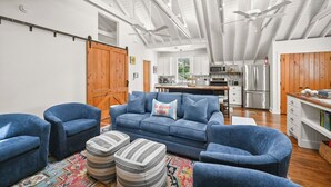 Ein großzügiger Wohnbereich mit blauem Sofa, Hocker und einer Küche im Hintergrund.