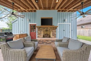Une terrasse extérieure aménagée avec des meubles en osier, une cheminée en pierre et des ventilateurs de plafond.