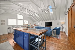 Un loft spacieux avec un plafond haut, un îlot central doté de meubles bleus, un canapé bleu et un téléviseur fixé au mur.