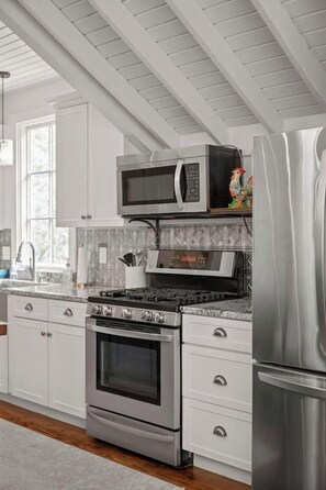Una cocina con armarios blancos, electrodomésticos de acero inoxidable y un ventanal que proporciona luz natural.