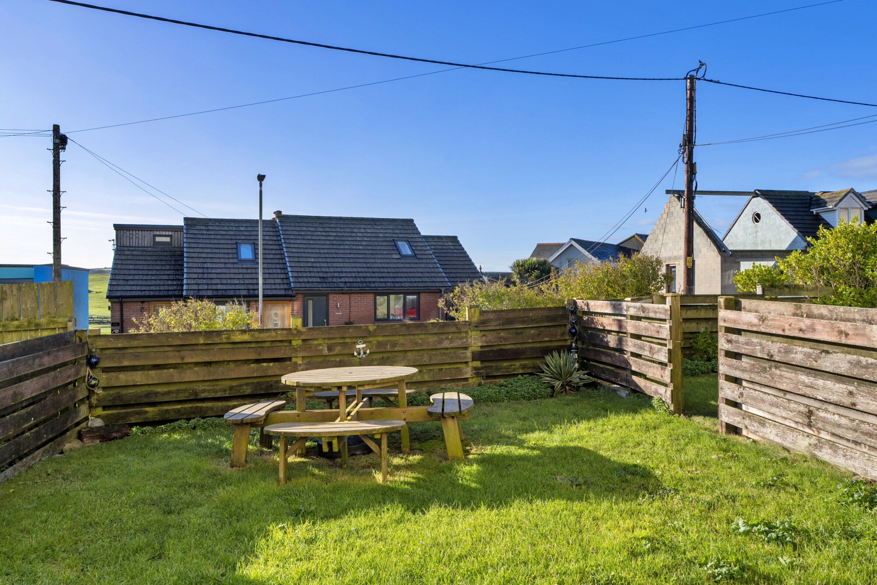 A grassy backyard with a wooden table and benches, surrounded by a wooden fence.