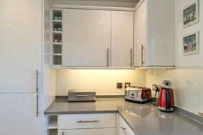 Eine Küche mit weißen Schränken, einem Toaster, einem Wasserkocher und einem kleinen Kühlschrank.