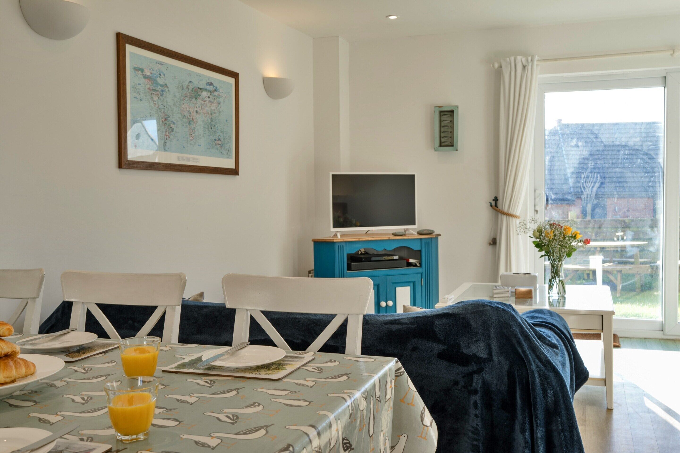 A dining area with a table set for breakfast, a television on a stand, and a view of the outdoors through a window.