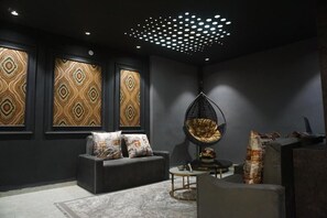 A modern living room with a dark grey sofa, patterned wall panels, a hanging chair, and a round coffee table. - The Havelock By EliteKeys (Indore)