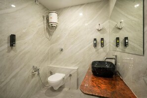 A modern bathroom with a marble wall, a black sink, a toilet, and a handheld showerhead. - The Havelock By EliteKeys (Indore)