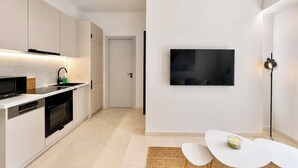 Een moderne keuken met inbouwapparatuur, een eethoek met een witte tafel, en een flatscreen televisie aan de wand bevestigd.