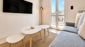 Een moderne woonkamer met een flatscreen televisie, een bank, een klein rond tafeltje en een vloerlamp.