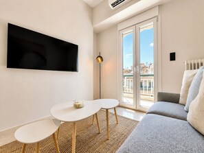 En moderne stue med et fladskærms TV, en sofa, et rundt sofabord og en gulvlampe.