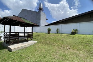 Eine Rasenfläche mit einer Betonkonstruktion, einem Pavillon mit Metallbedachung und einem Wassertank im Hintergrund.