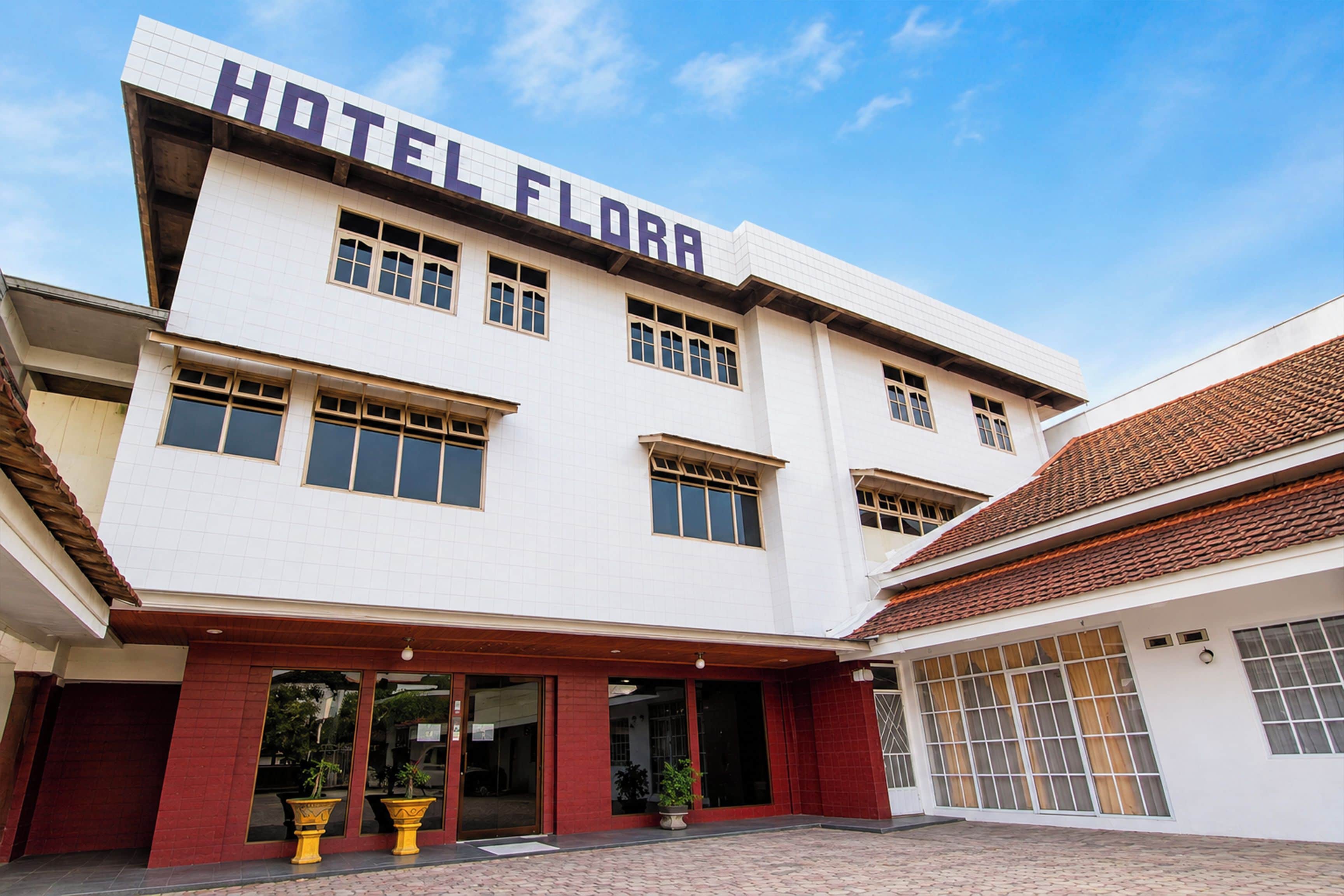 Et hotel med et tydeligt skilt, der siger 'HOTEL FLORA', flere vinduer og en fliset indgang.