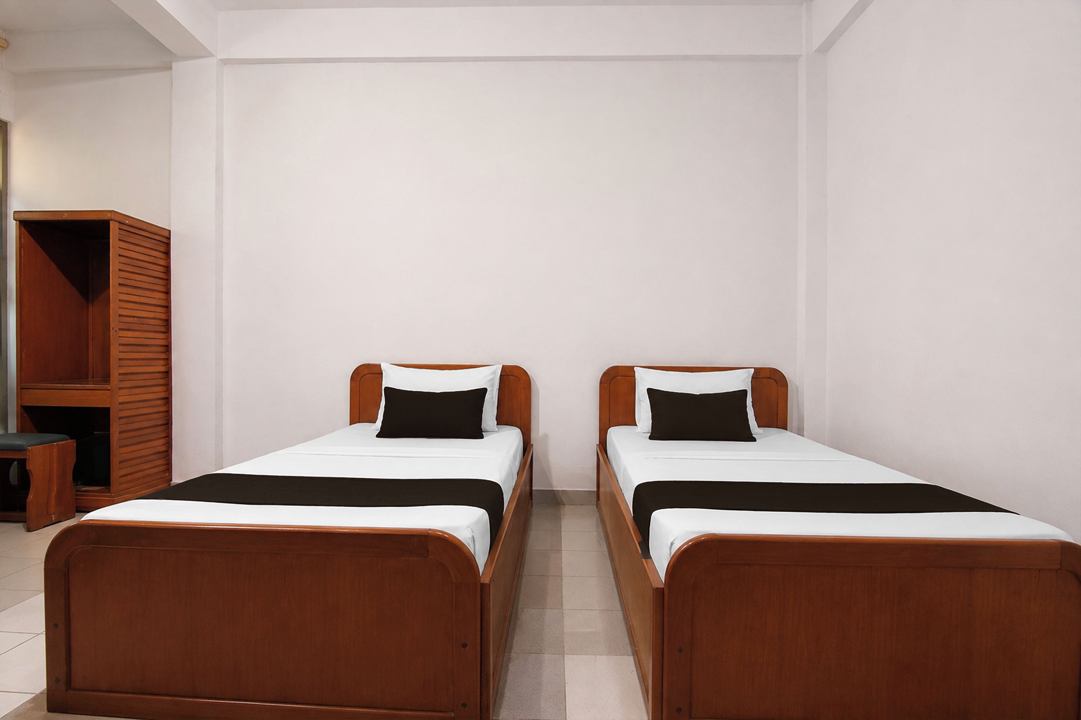 Ein Zimmer mit zwei Holzbetten, jeweils mit weißer Matratze und schwarzen Kissen, sowie einem Holzschrank.