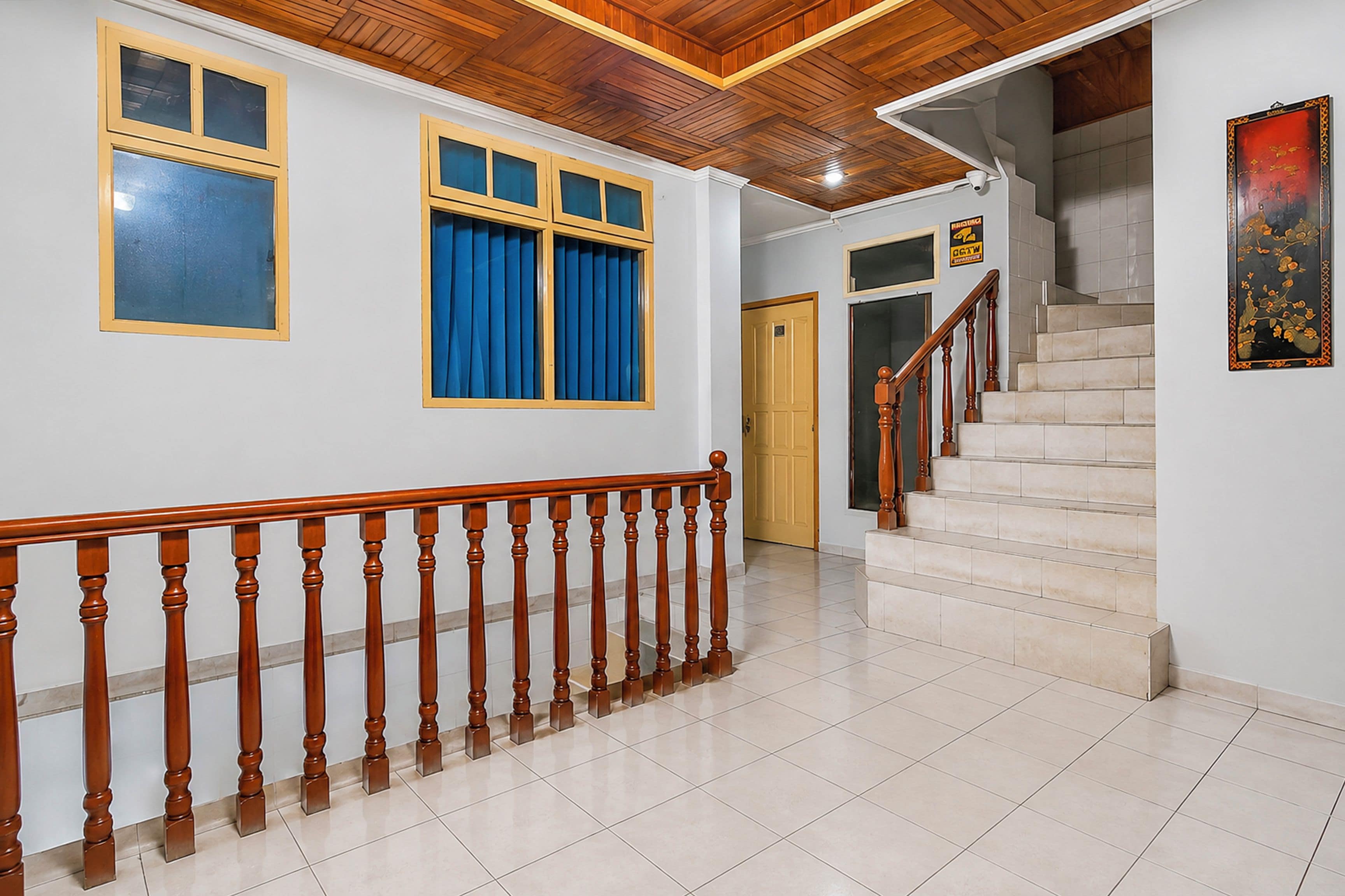 Uma escadaria de madeira com balaústres leva a um patamar, uma porta com uma placa acima e uma janela com cortinas azuis.