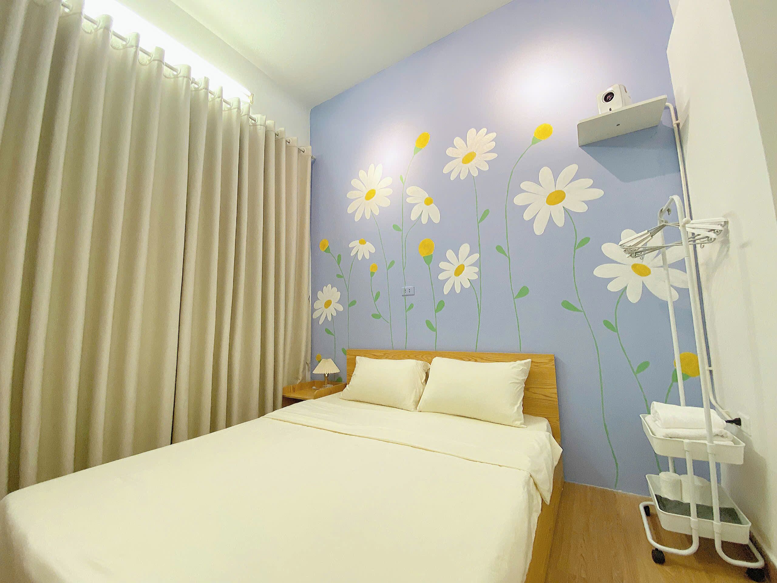 A bedroom with a bed, curtains, a nightstand, a lamp, a wall-mounted air conditioner, and a white bedside table with a tray.