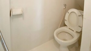 Een kleine, witte badkamer met toilet, douche en ventilatie.
