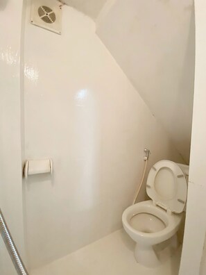 Ein kleines, weißes Badezimmer mit Toilette, Dusche und Abluftventilator.