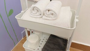 Een witte, verplaatsbare sanitaire kar met een handdoekhouder en een prullenbak.