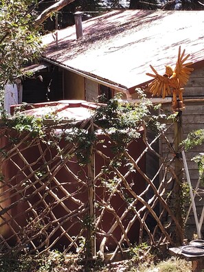 Une clôture en bois ornée de plantes grimpantes, une petite construction en bois avec un toit rouge et un moulin à vent décoratif.