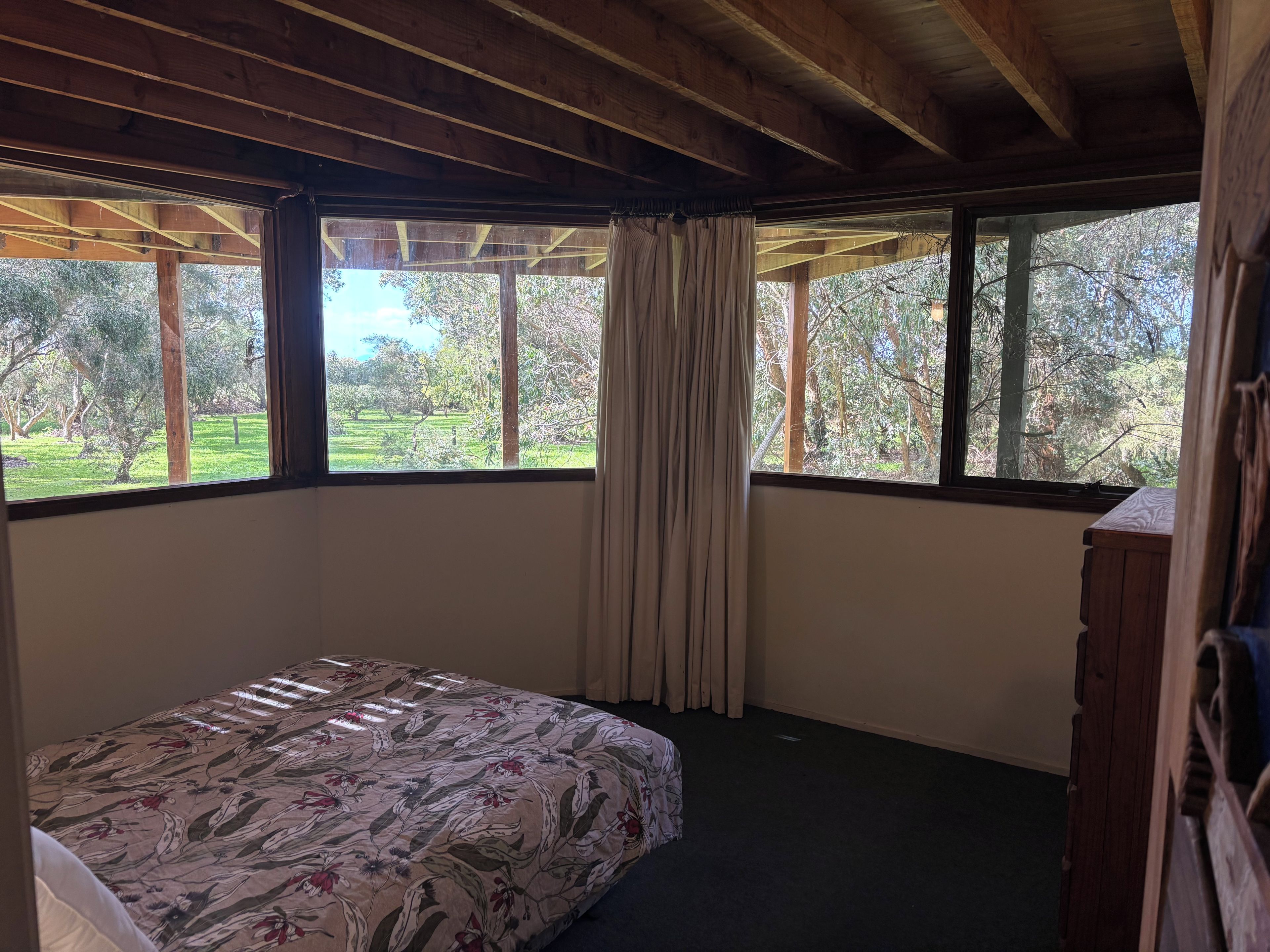 Une chambre à coucher avec un lit, une commode en bois et une fenêtre avec des rideaux.