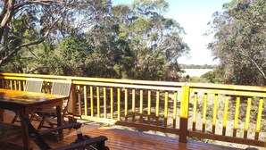 A wooden deck with a table and chairs, surrounded by a railing, overlooking a natural landscape.