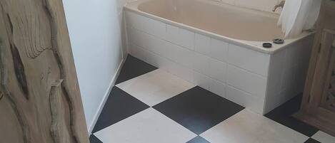 A bathroom with a checkered floor, a bathtub, and a window.