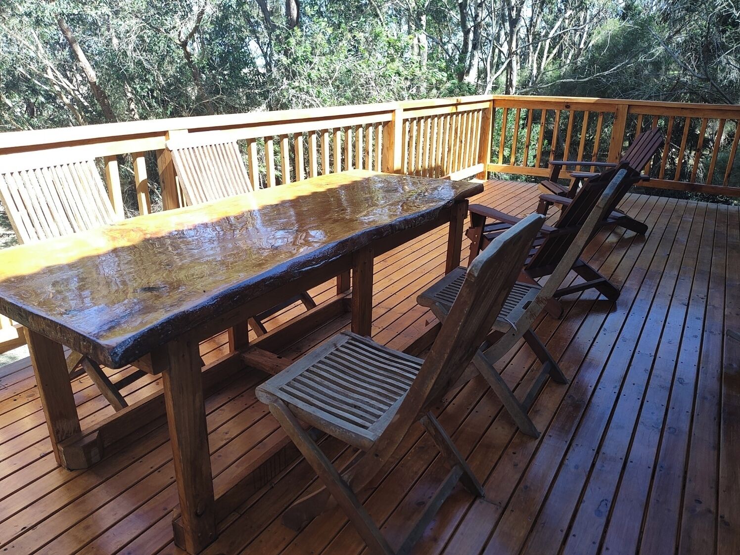 Una terraza de madera con mesa y sillas, rodeada de árboles.