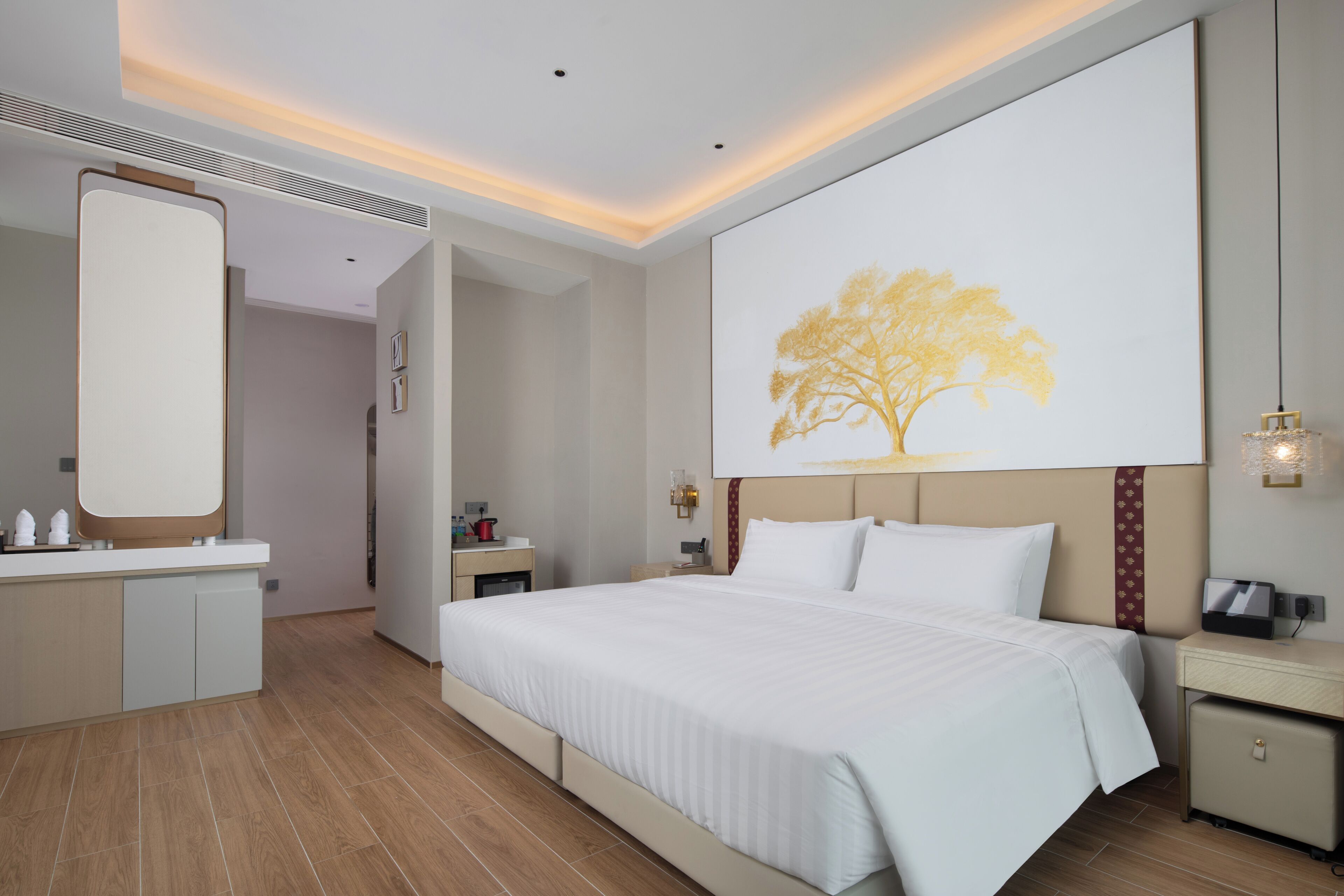 A modern hotel room with a large bed, a bedside table, a nightstand, a mirror, and a wall-mounted artwork.