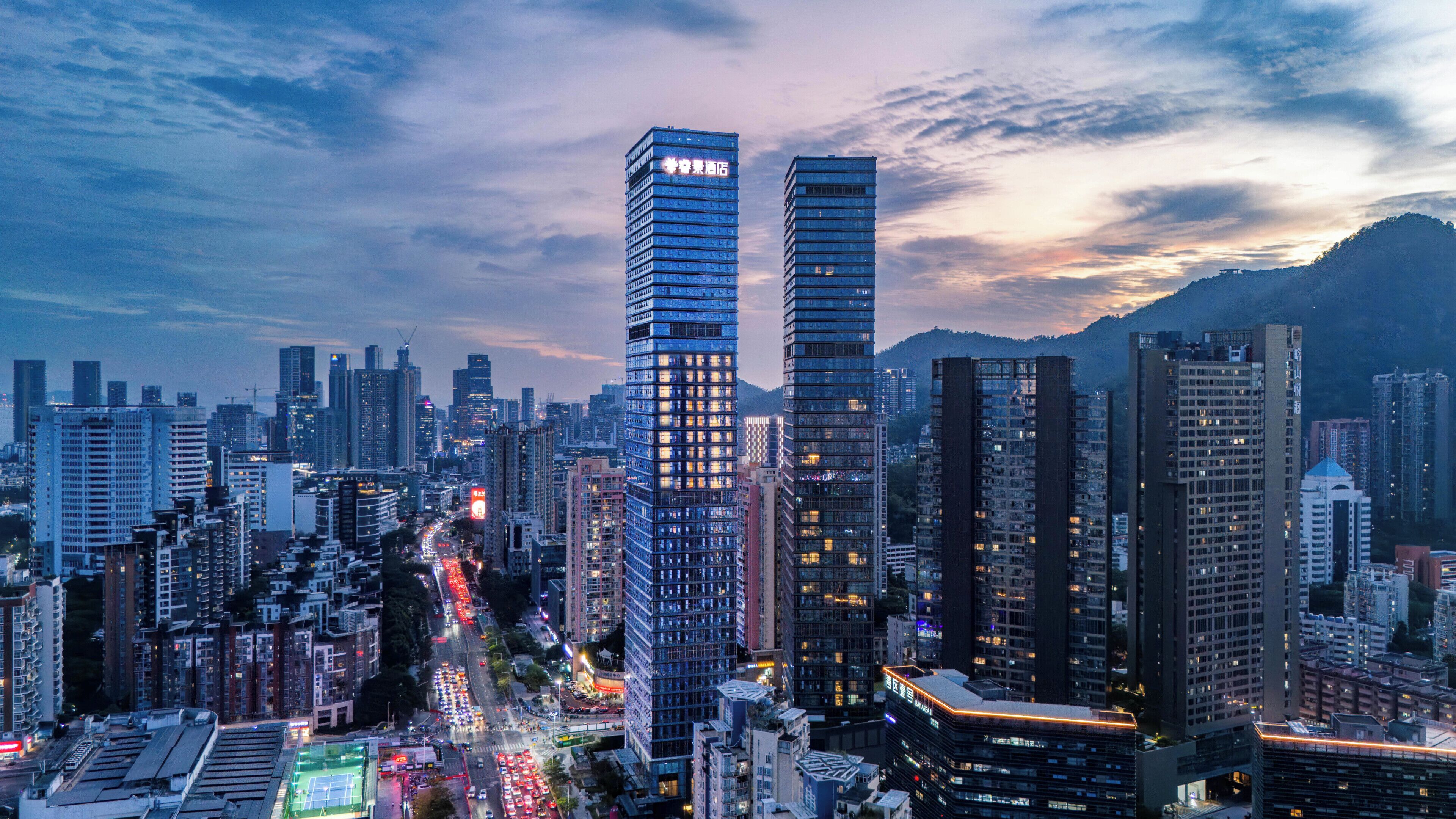 A cityscape with multiple high-rise buildings, including two prominent skyscrapers with illuminated windows.