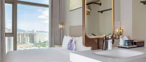 Habitación de hotel con una cama grande, un baño con lavamanos moderno y vista a la ciudad desde la ventana.