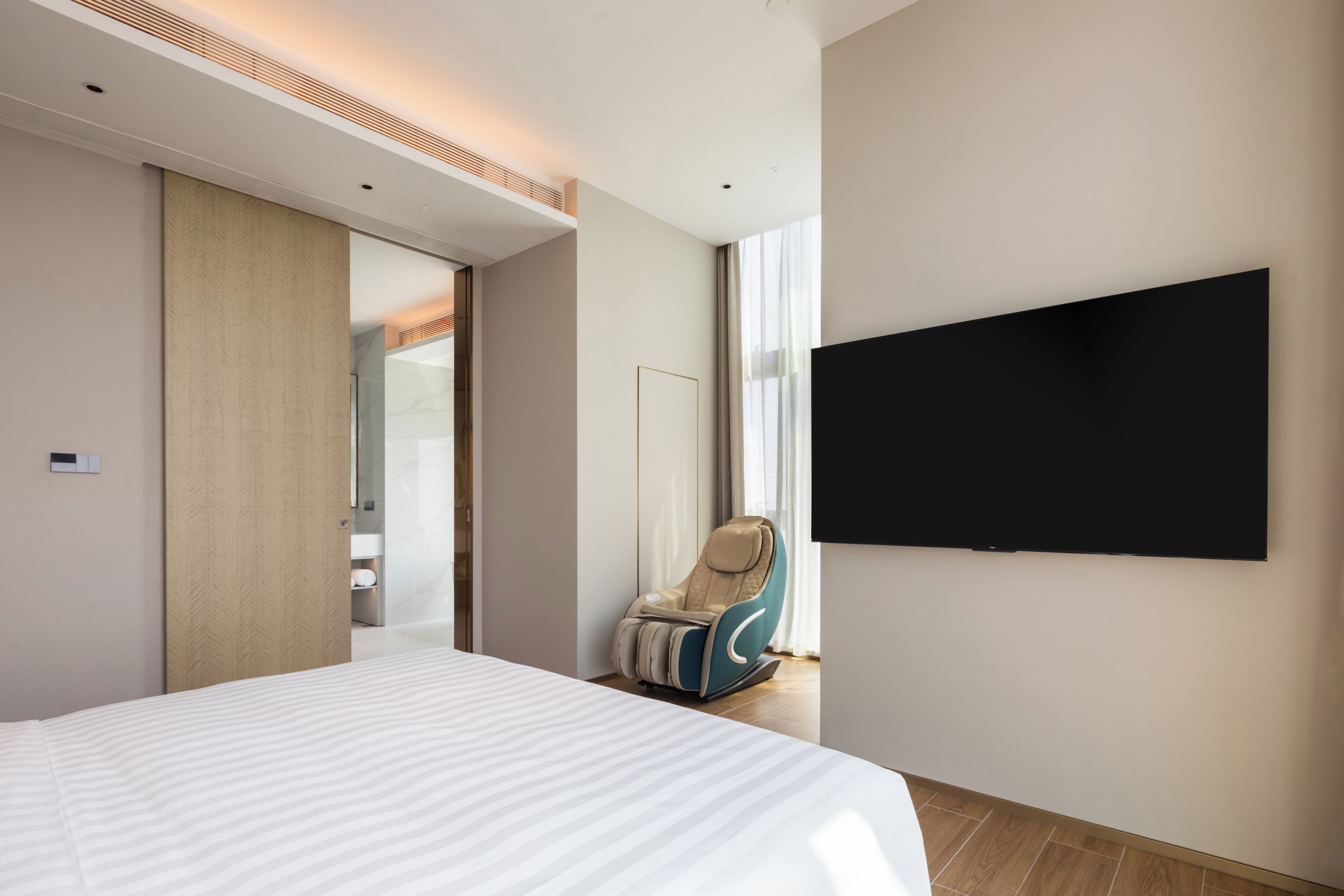 Una habitación de hotel moderna con una cama grande, una silla de masaje, un televisor de pantalla plana y un vestidor.