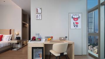 Una habitación de hotel moderna con una cama, un escritorio con una silla, un mini refrigerador y obras de arte en las paredes.