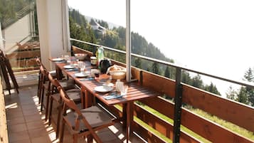 Une terrasse en bois avec une table à manger pour quatre personnes, offrant une vue sur un paysage montagneux.