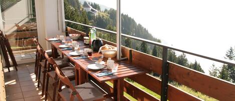 A wooden deck with a dining table set for four, overlooking a mountainous landscape.